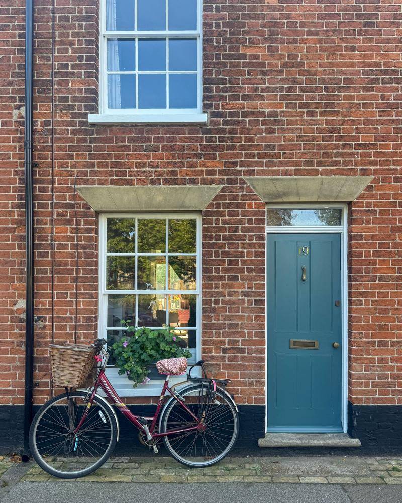 The front of a red brick house with a pale blue front door and a bicycle leaning against the wall