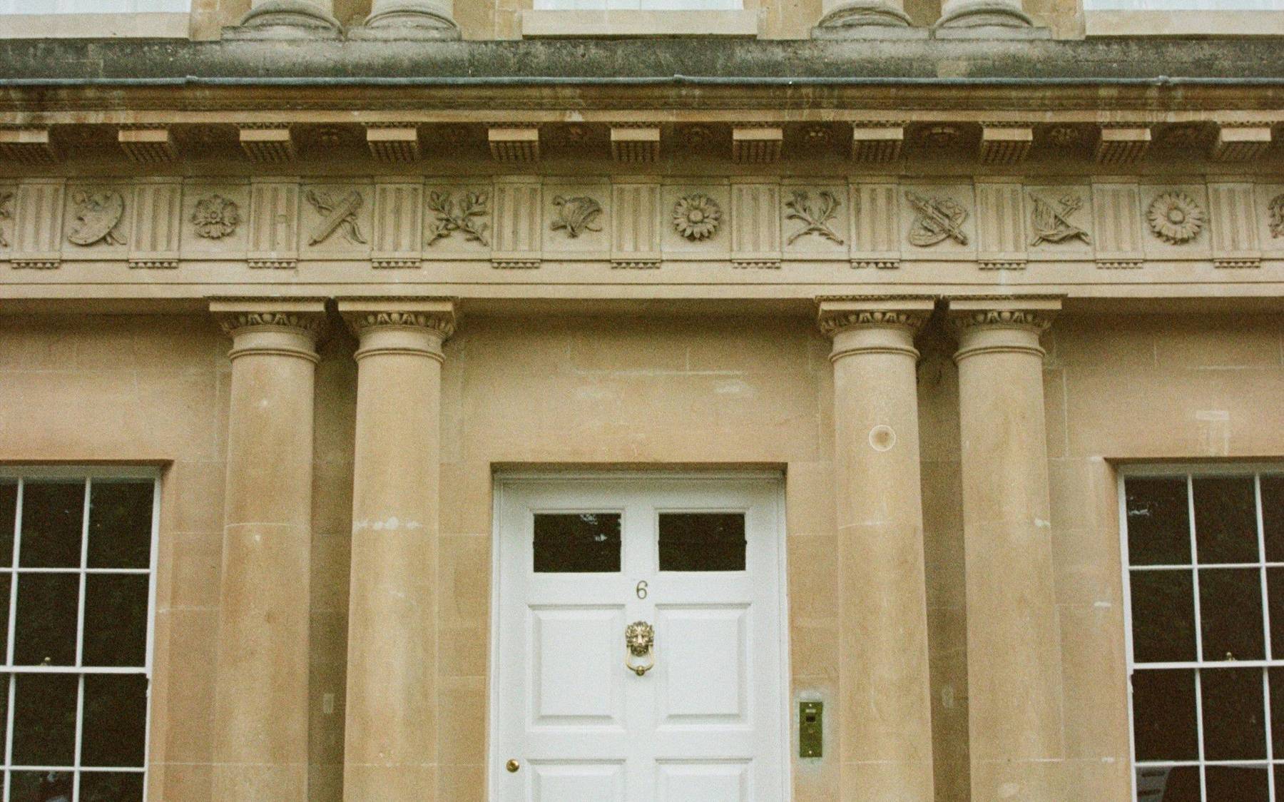 The symmetrical stone front of a Georgian townhouse with a white front door and iron railings