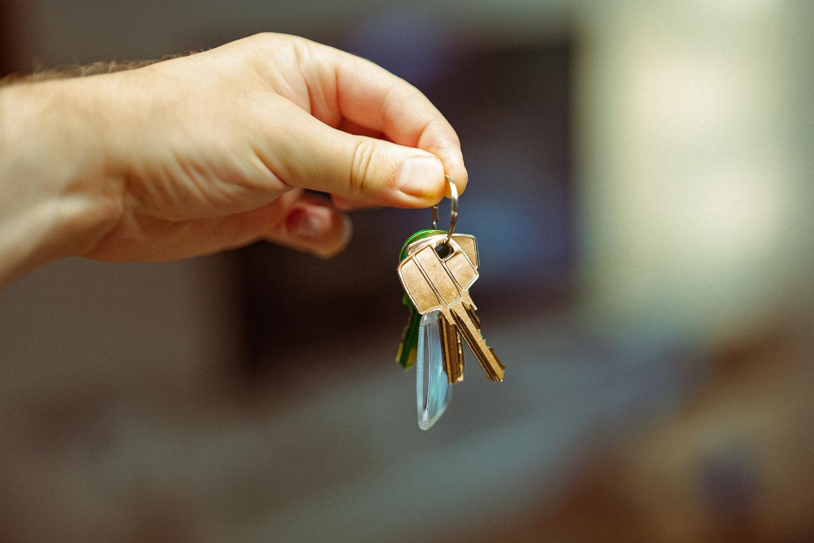 A hand holding a bunch of house keys on a ring, with a blurred room behind