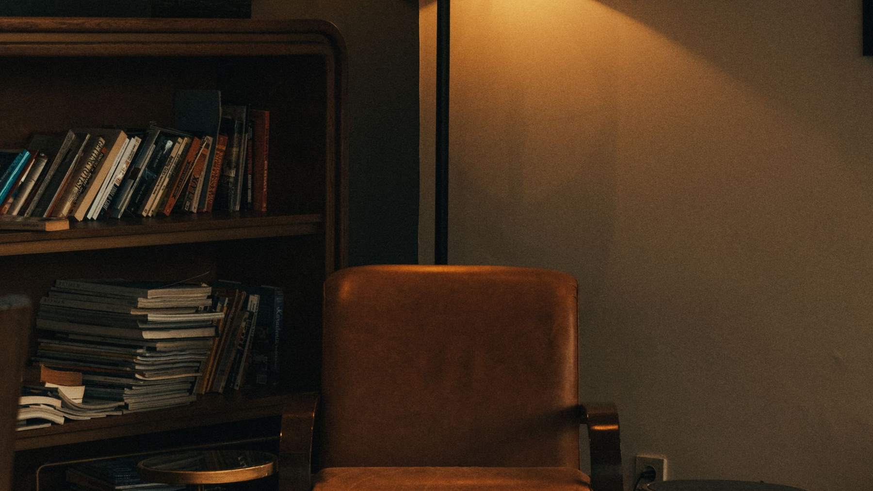 A leather armchair beside a lamp and a bookshelf in a warmly lit room