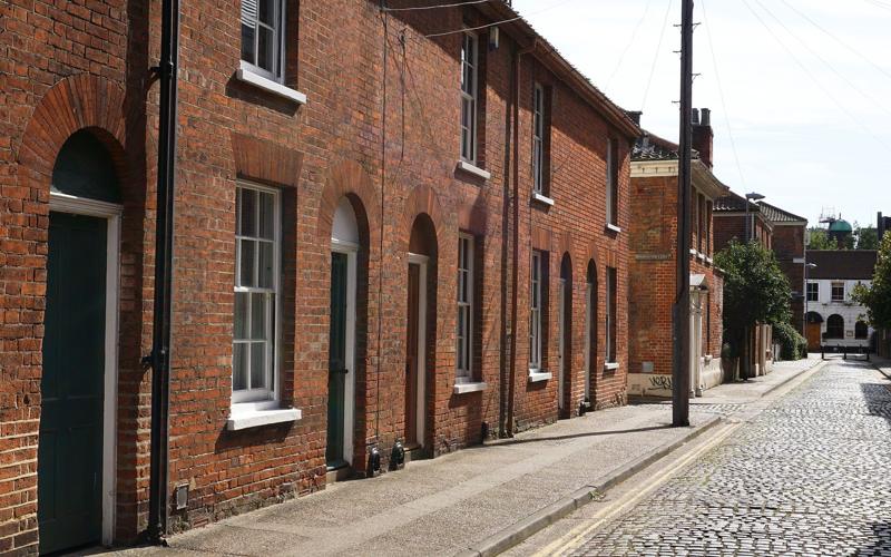 A cobbled street in Norwich lined with brick houses and pale painted window frames