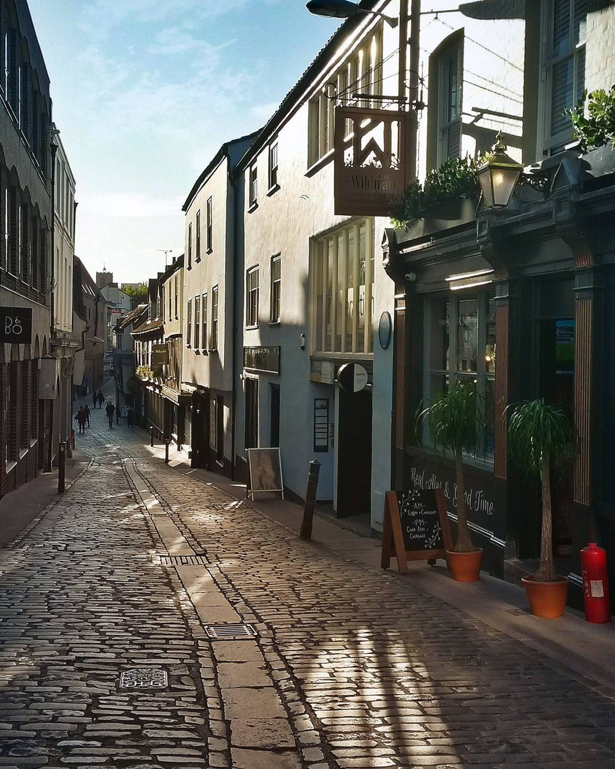 A narrow cobbled street in Norwich in low morning light, with old buildings either side