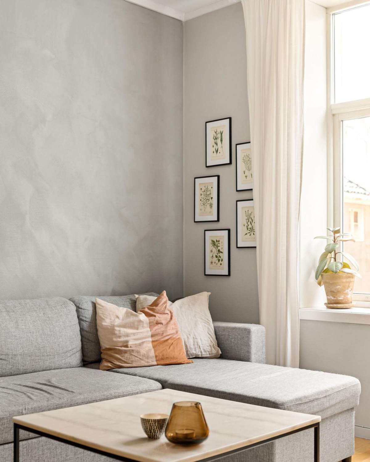 A simple living room with a grey sofa, a wooden coffee table and framed prints on a pale wall