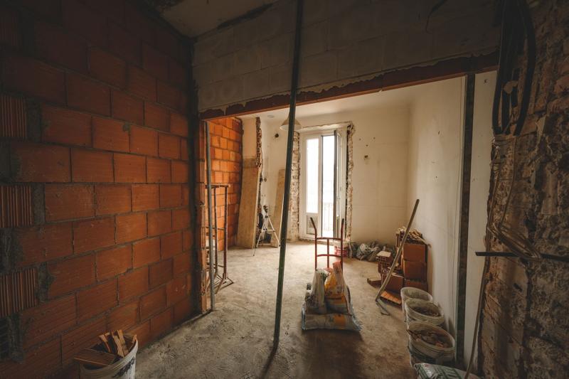 A room stripped back to bare brick during a refurbishment, with a window at the far end and tools on the floor